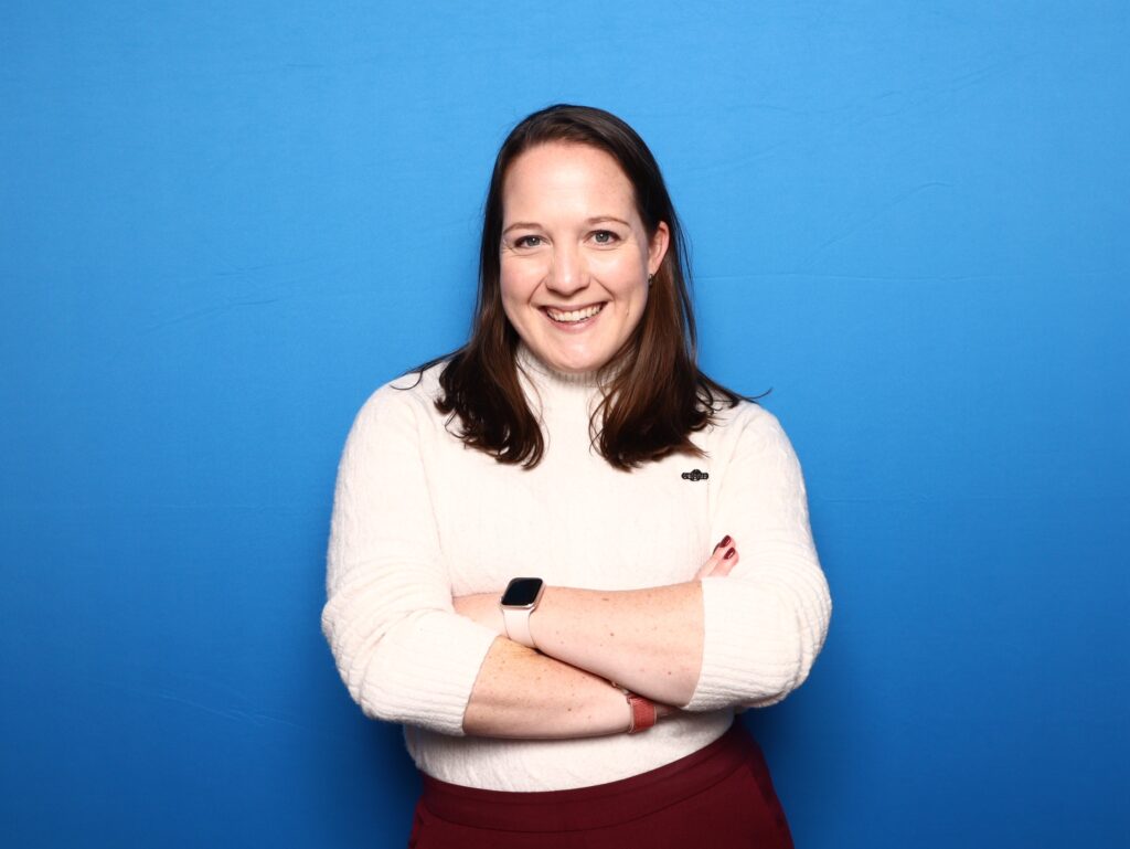 Photo of Dr. Shelby Scott, showing a person wearing a white sweater with arms crossed on a blue background
